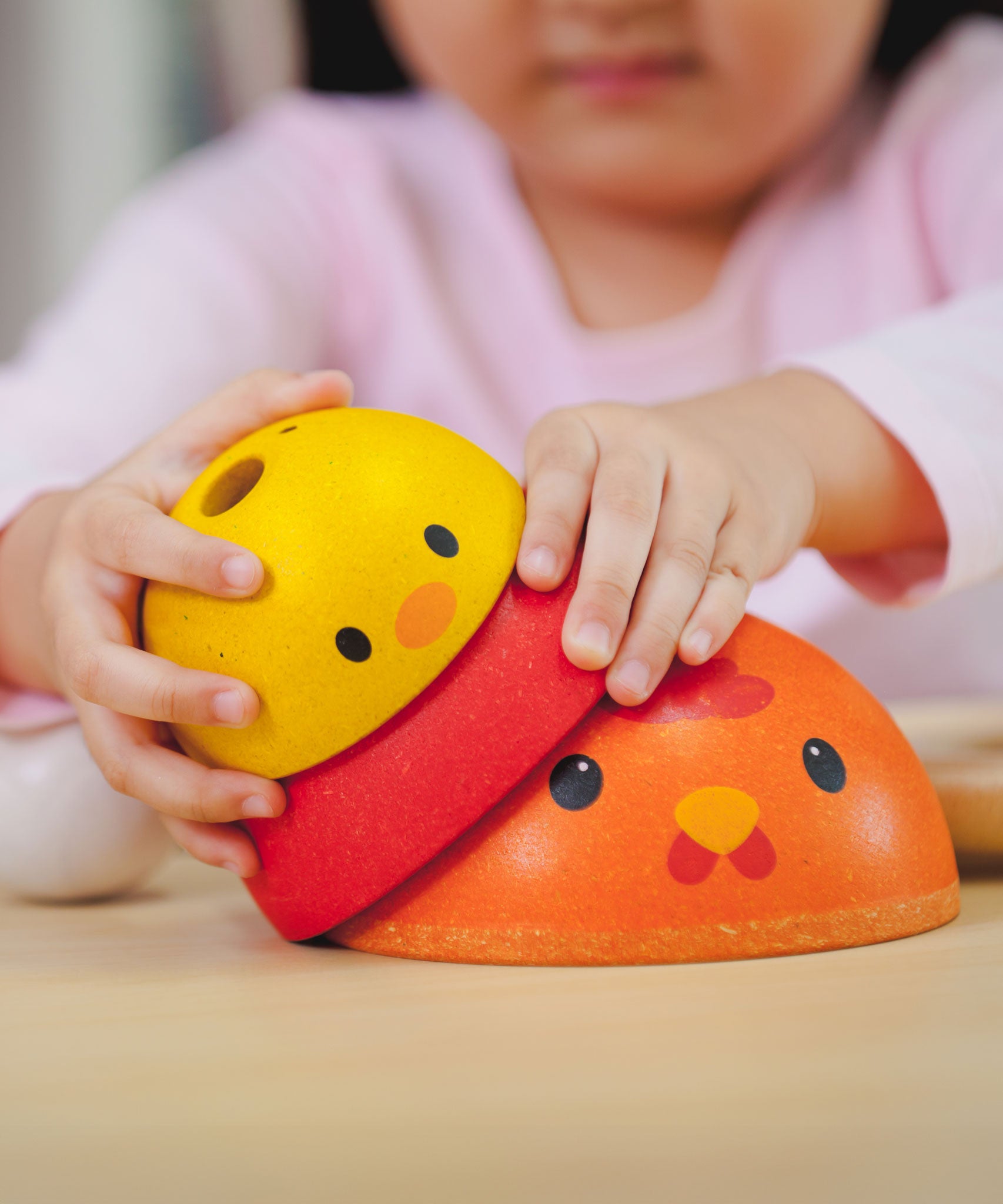 A close up of a child's hands playing with the PlanToys Chicken Nesting Toy. 