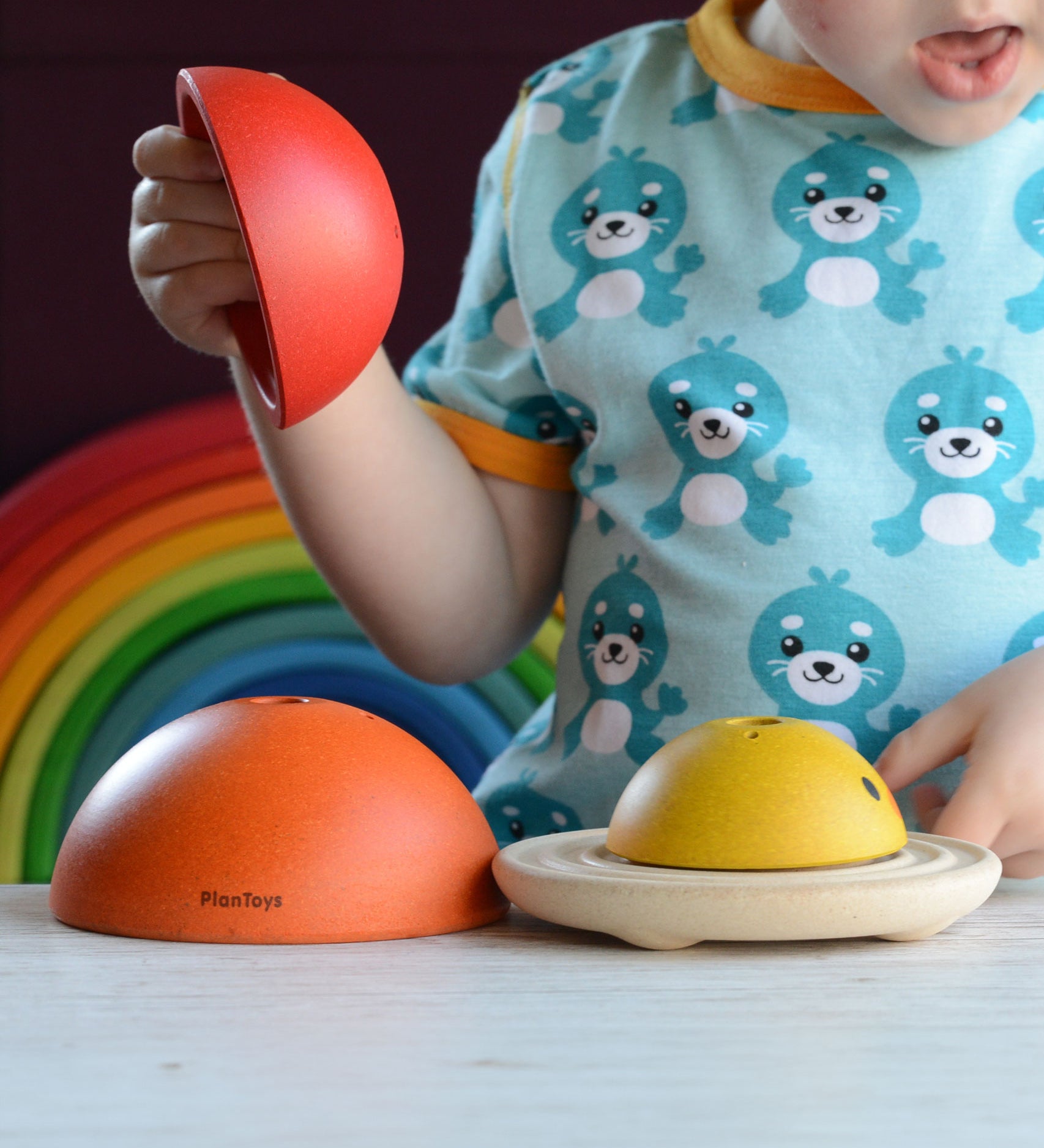 A child playing with the PlanToys Chicken Nesting Toy. A Grimm's rainbow can be seen behind them. 