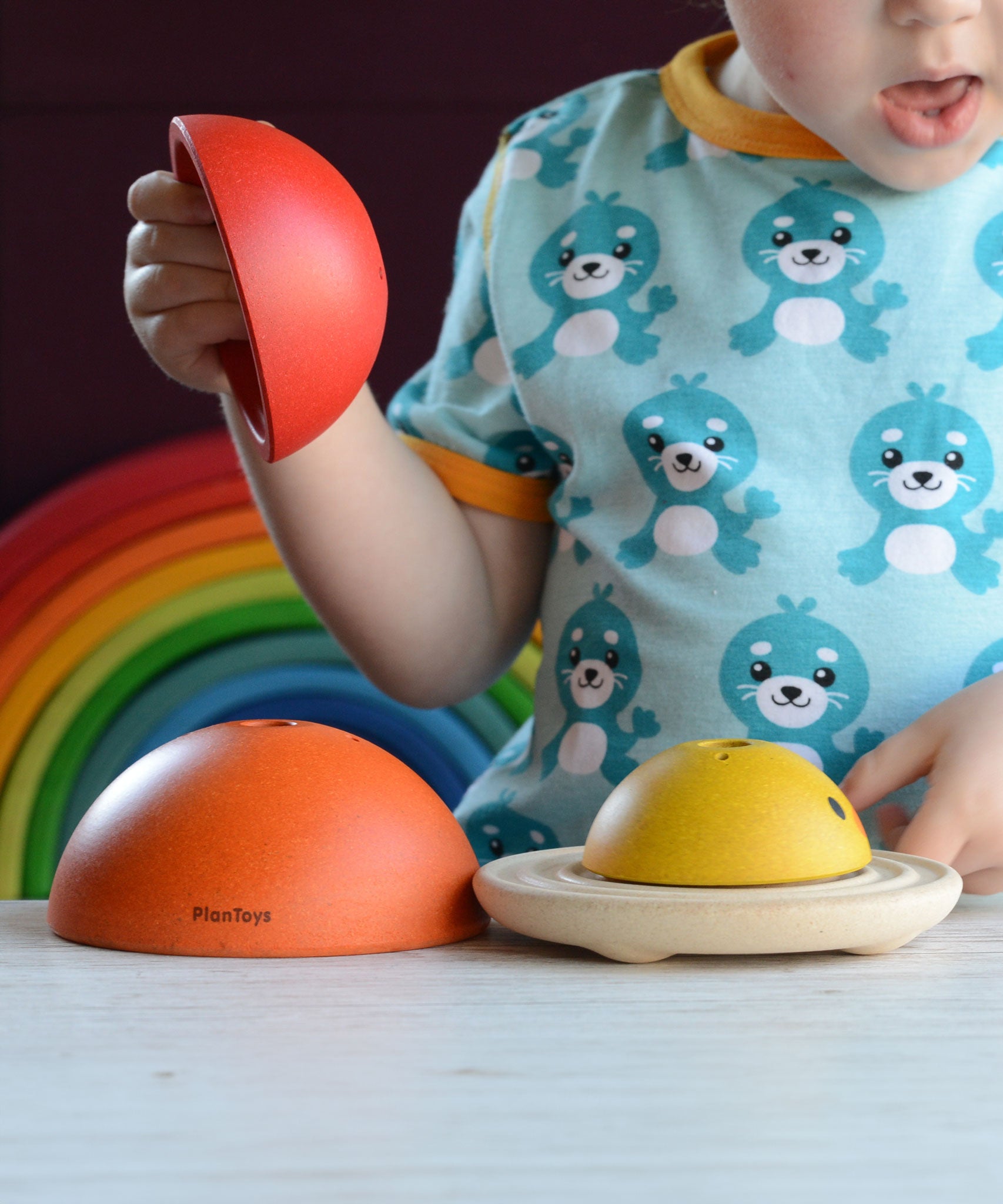 A child playing with the PlanToys Chicken Nesting Toy. A Grimm's rainbow can be seen behind them. 