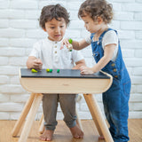 A child sitting by a PlanToys Black Table & Chair. Another child is standing by their side.