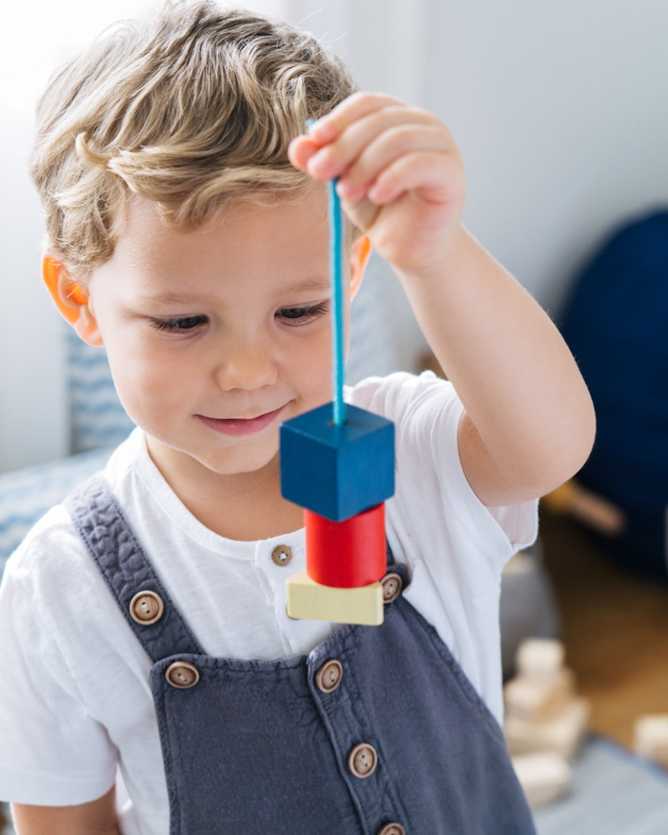 Close up of a child holding up some wooden PlanToys geo lacing blocks in front of his face