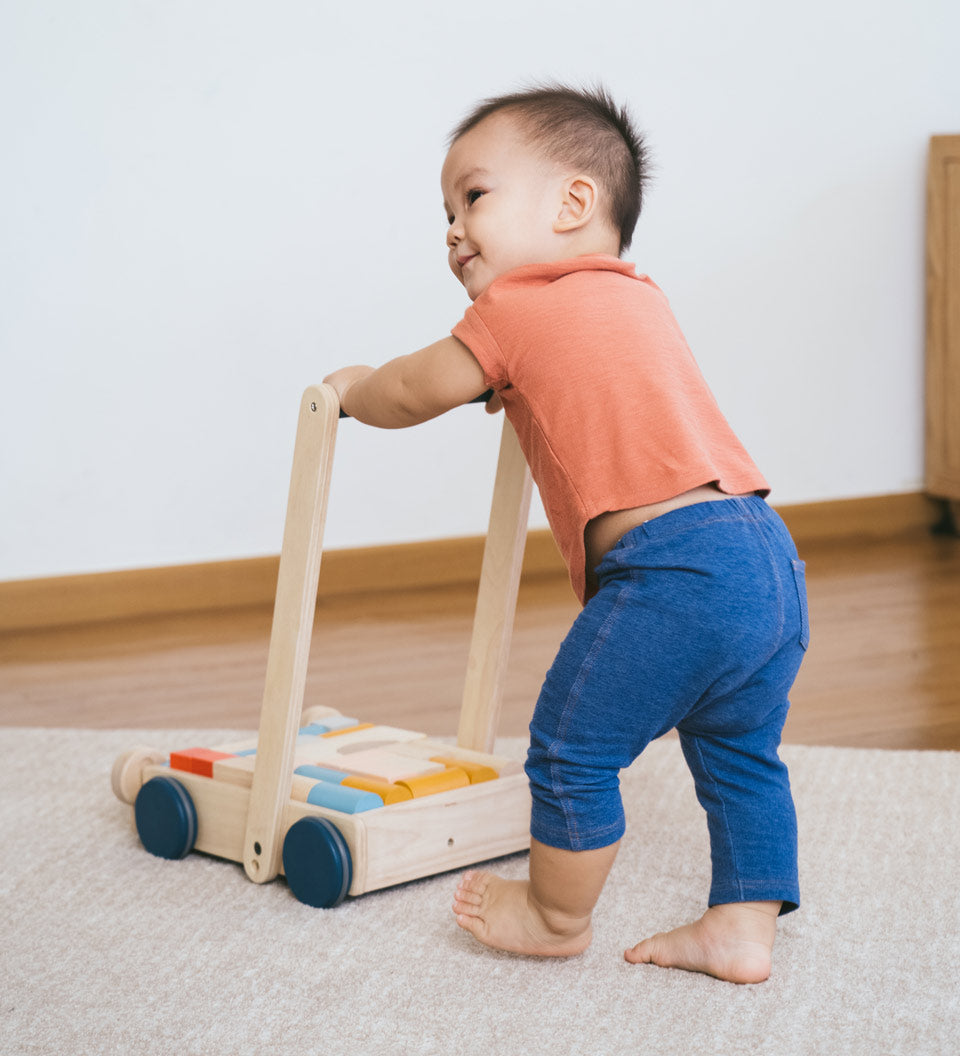 Young toddler walking around holding the Plan Toys eco-friendly wooden baby walker