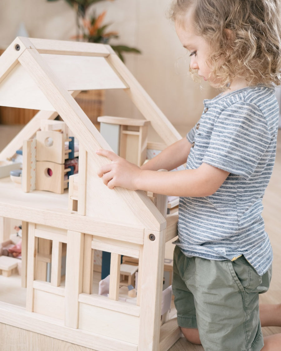 Close up of young child playing with toy dolls inside the PlanToys plastic-free first dolls house toy set