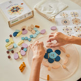 Close up of some hands arranging the PlanToys wooden mandala toy blocks on a white table cloth