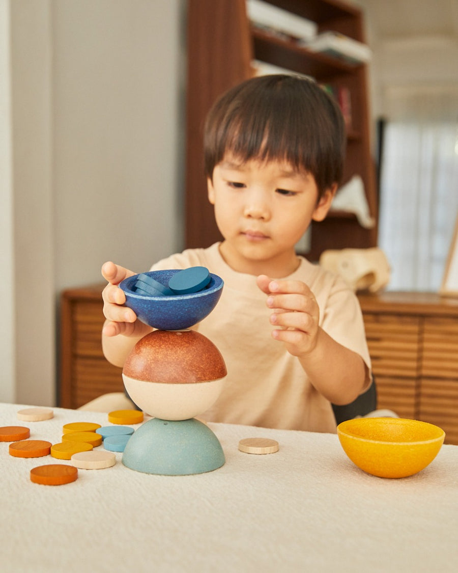 Young child stacking the PlanToys wooden orchard sort and count cups on a table