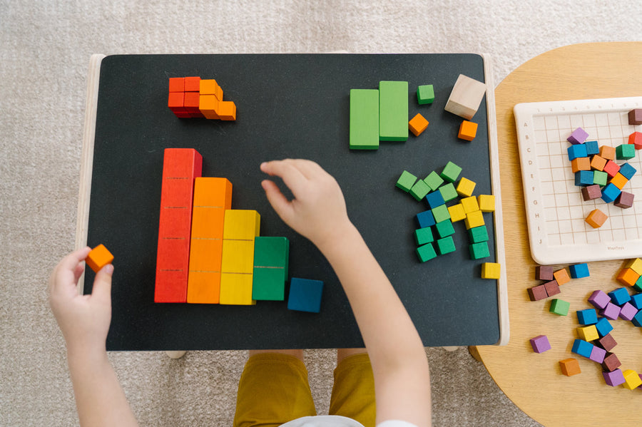 Close up of a child's hands sorting the PlanToys rainbow coloured counting cubes on a black table