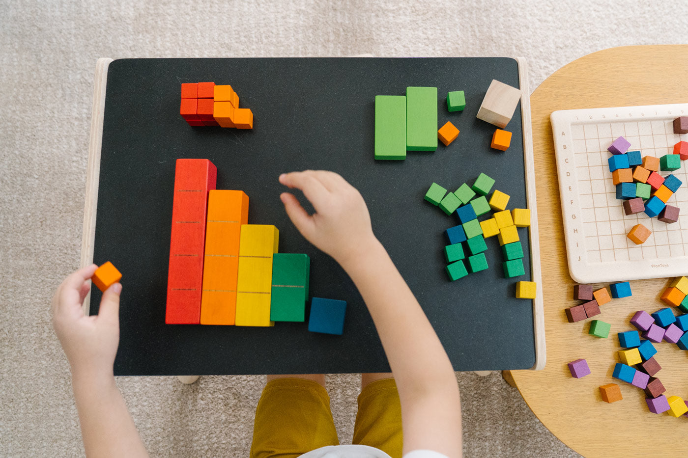 Close up of a child's hands sorting the PlanToys rainbow coloured counting cubes on a black table