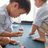 Close up of young boy crouched on a blue carpet hooking the PlanToys wooden fish toy with a toy fishing rod