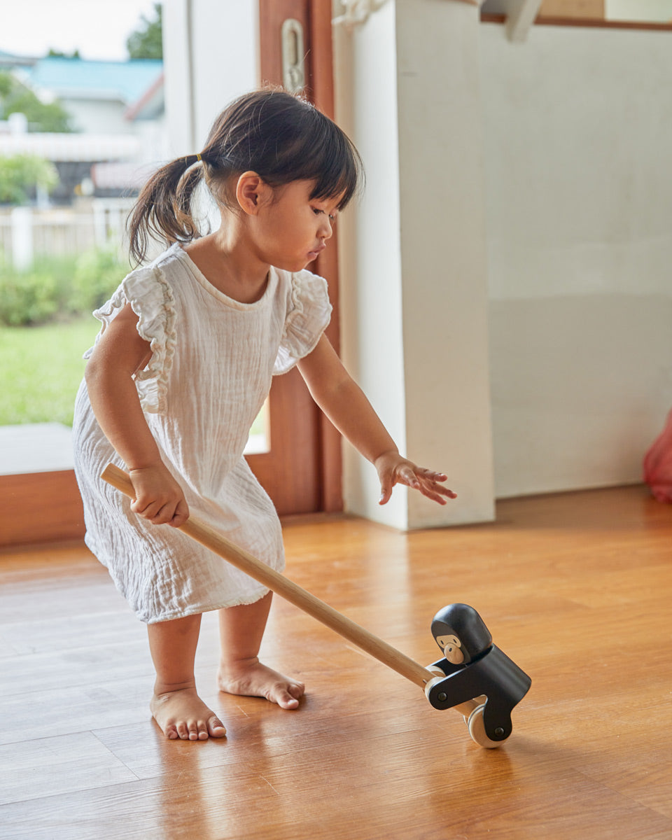 Girl reaching down to grab the PlanToys wooden climbing gorilla pull along toy