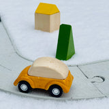 Yellow wooden car on the PlanToys eco-friendly rubber road and rail toy set on a white background