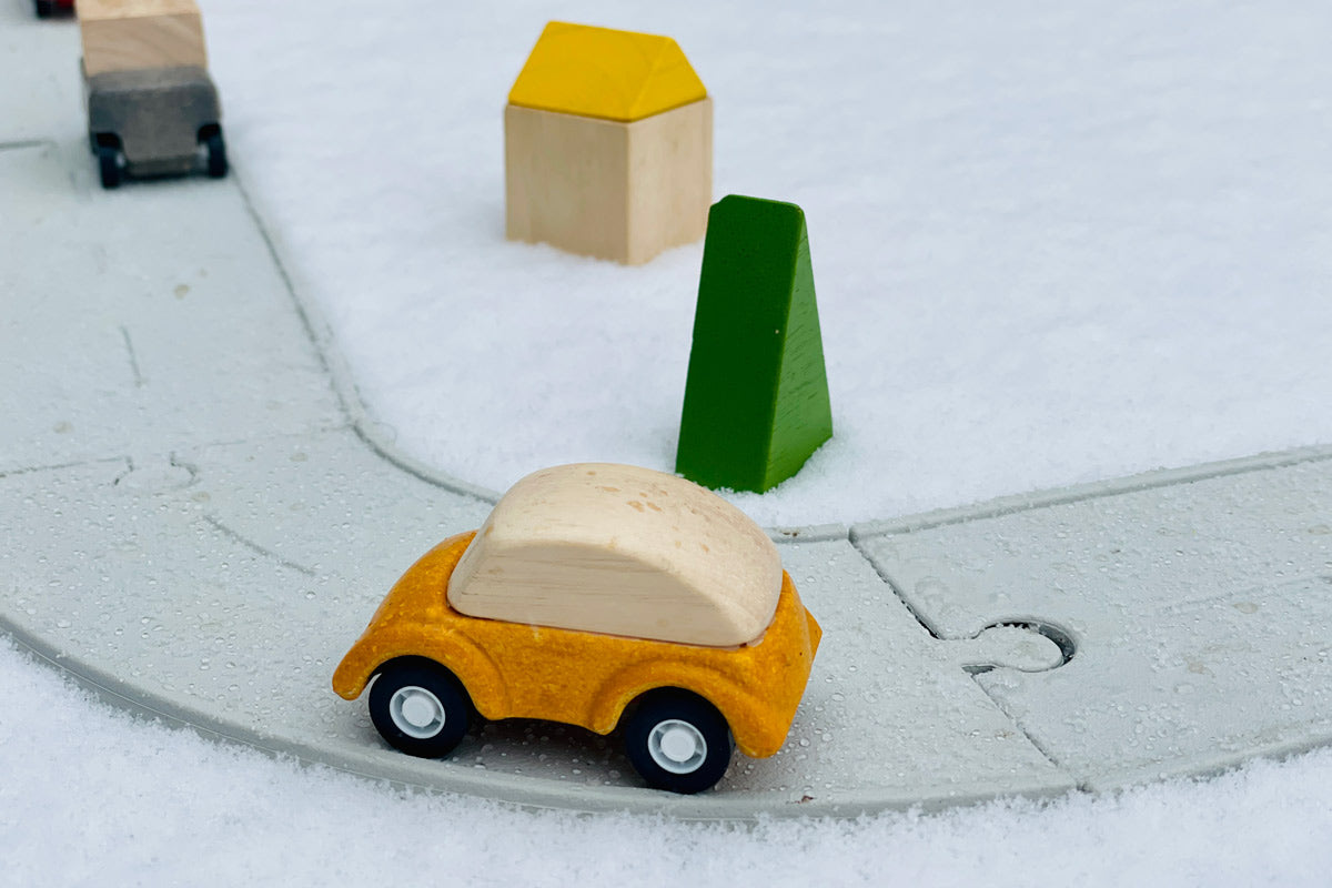 Yellow wooden car on the PlanToys eco-friendly rubber road and rail toy set on a white background