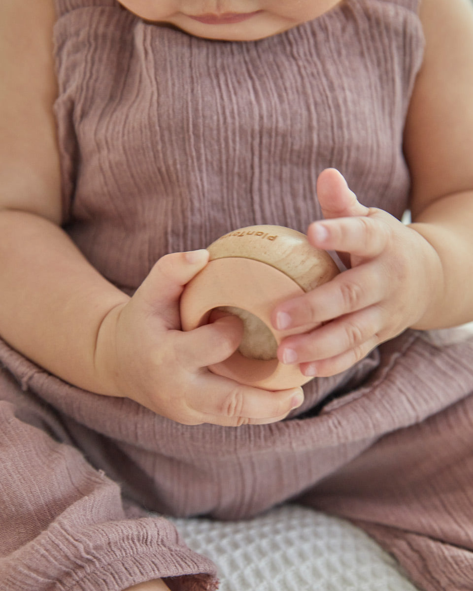 Young toddler sat on a white bed holding the PlanToys wooden sensory tumbling balls