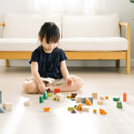 Young girl sat on the floor playing with the PlanToys stacking wooden countryside blocks