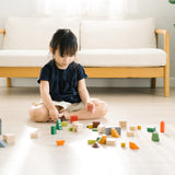 Young girl sat on the floor playing with the PlanToys stacking wooden countryside blocks