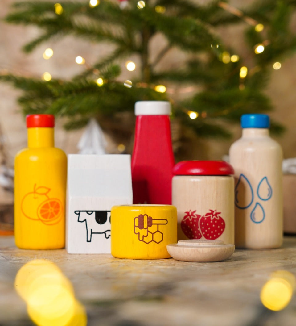 Close up of the PlanToys plastic-free wooden food and beverage play set in front of a small Christmas tree