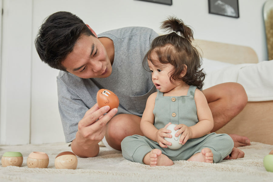 Young child and man sat on a fluffy carpet looking at the PlanToys plastic-free wobbly walrus toy