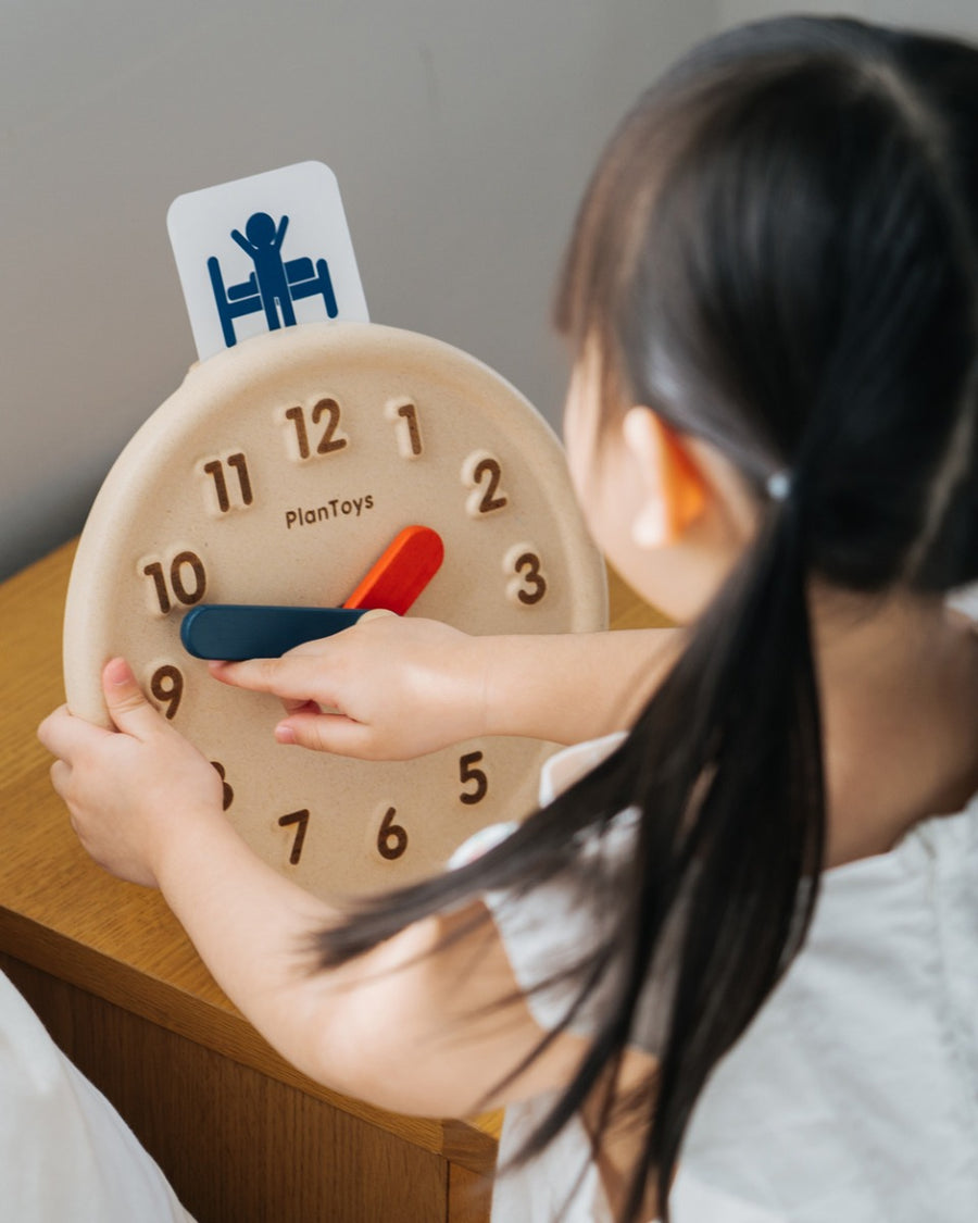 Close up of young girl turning the hands on the PlanToys plastic-free wooden activity clock