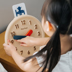 Close up of young girl turning the hands on the PlanToys plastic-free wooden activity clock