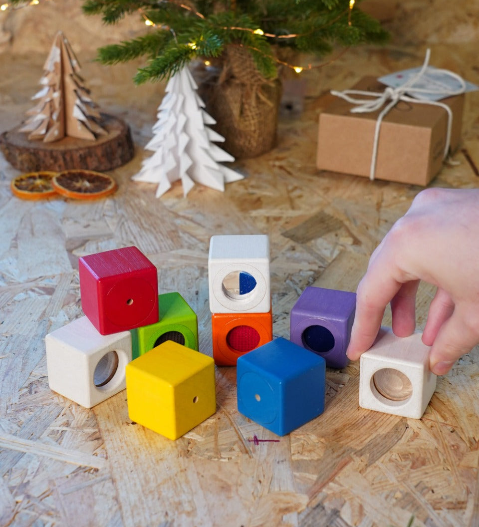 Close up of hand grabbing a white block from the PlanToys kids wooden sensory activity blocks in front of a small Christmas tree.