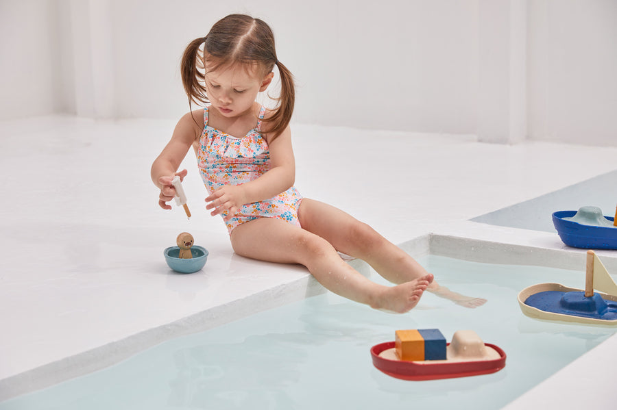 Girl sat on the edge of a swimming pool playing with the PlanToys wooden walrus sailing boat water toy