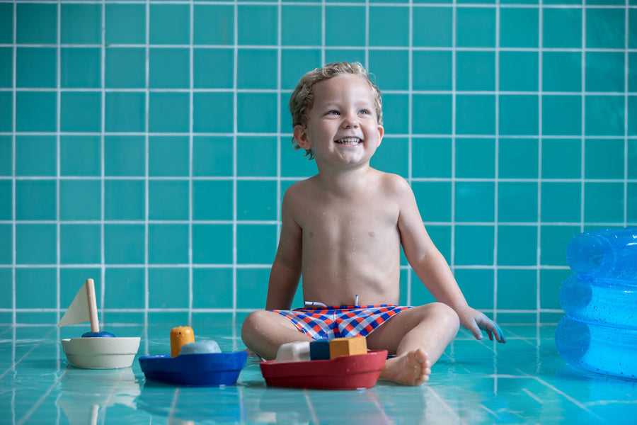 Young boy sat on some blue tiles playing with the PlanToys plastic-free tugboat