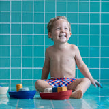 Young boy sat on some blue tiles playing with the PlanToys plastic-free tugboat