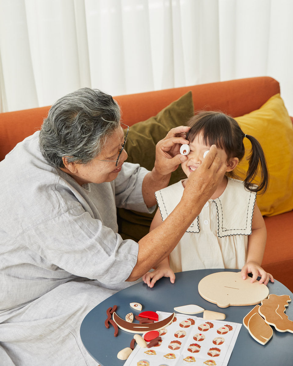 Woman holding up some toy wooden eyes up in front of a young girls face while she laughs