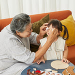 Woman holding up some toy wooden eyes up in front of a young girls face while she laughs