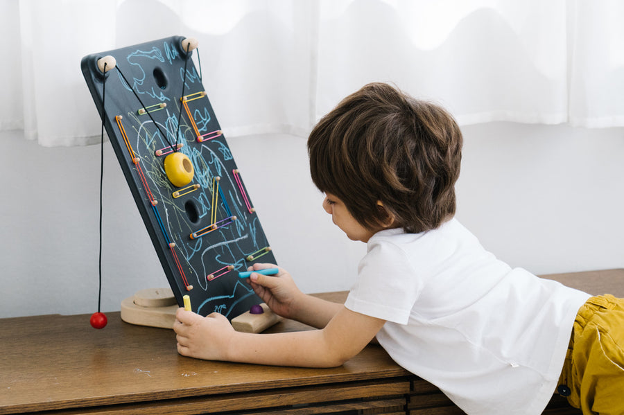 Child leaning over and drawing with a chalk on the PlanToys wooden wall ball game board