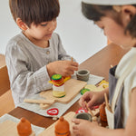 Close up of a young boy stacking food from the PlanToys wooden cheese and charcuterie play food set