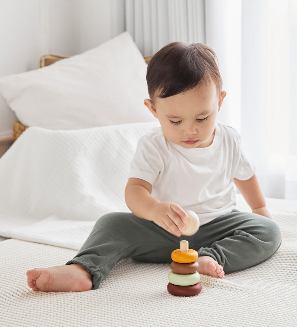 Young boy playing with the PlanToys Waldorf stacking rings toy on a white bed