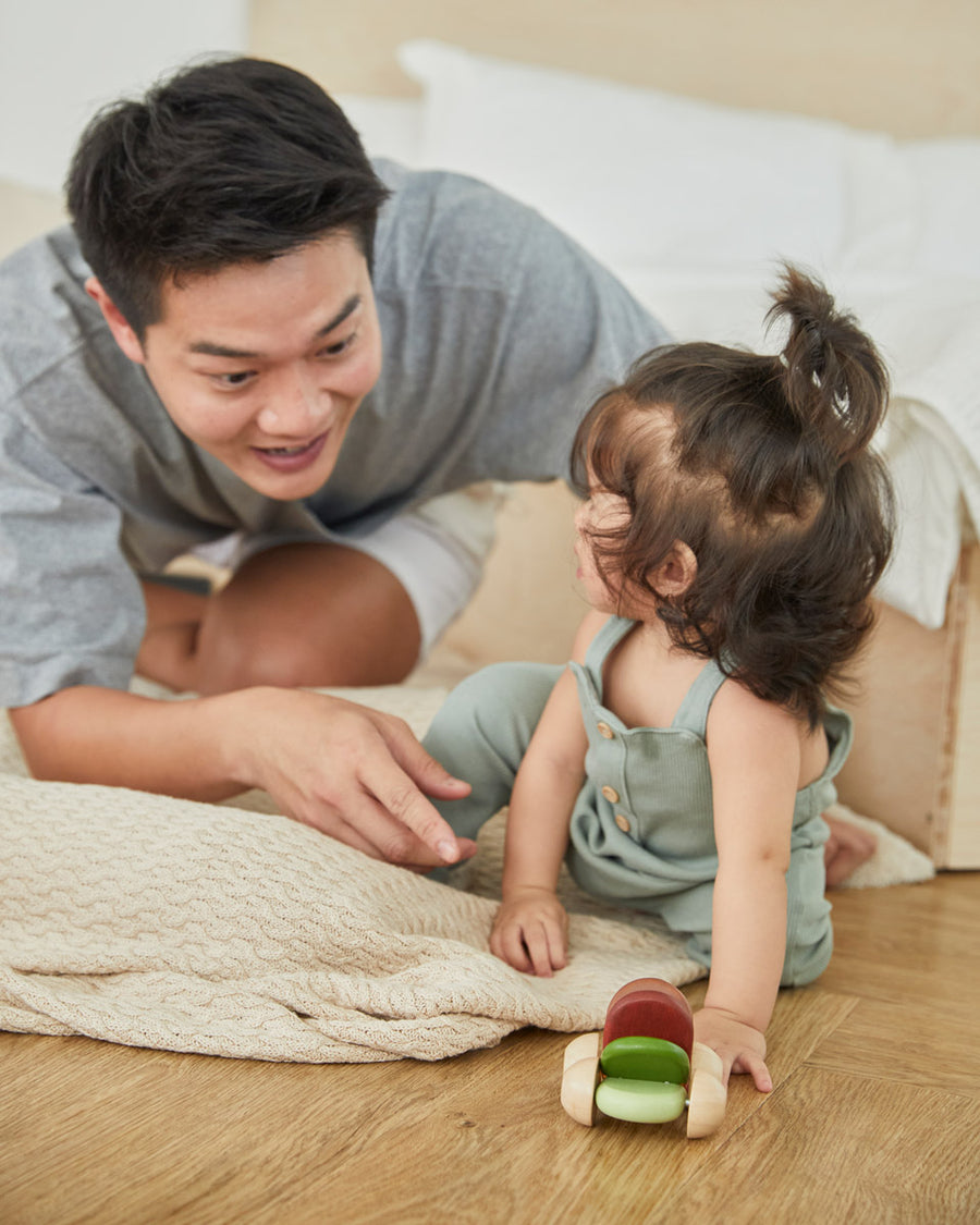 Young girl and man laying on a blanket playing with the PlanToys modern rustic plastic-free baby car toy