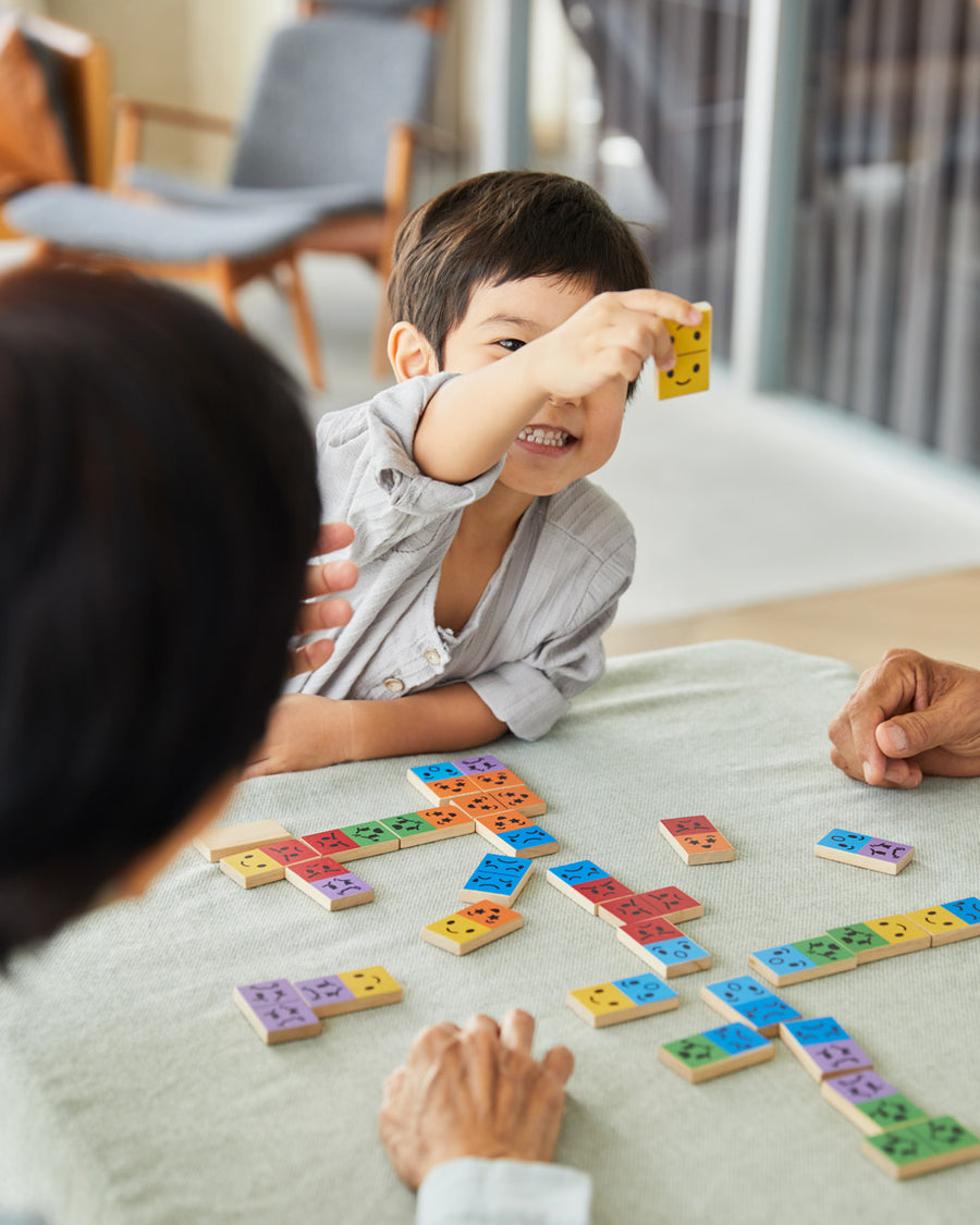 Young boy smiling and holding up a piece of the PlanToys wooden mood dominos game