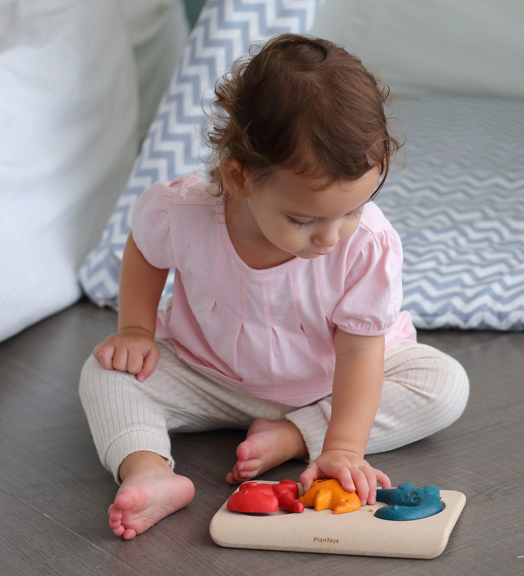 A child playing with PlanToys Dino Puzzle, child is sat on the floor. 