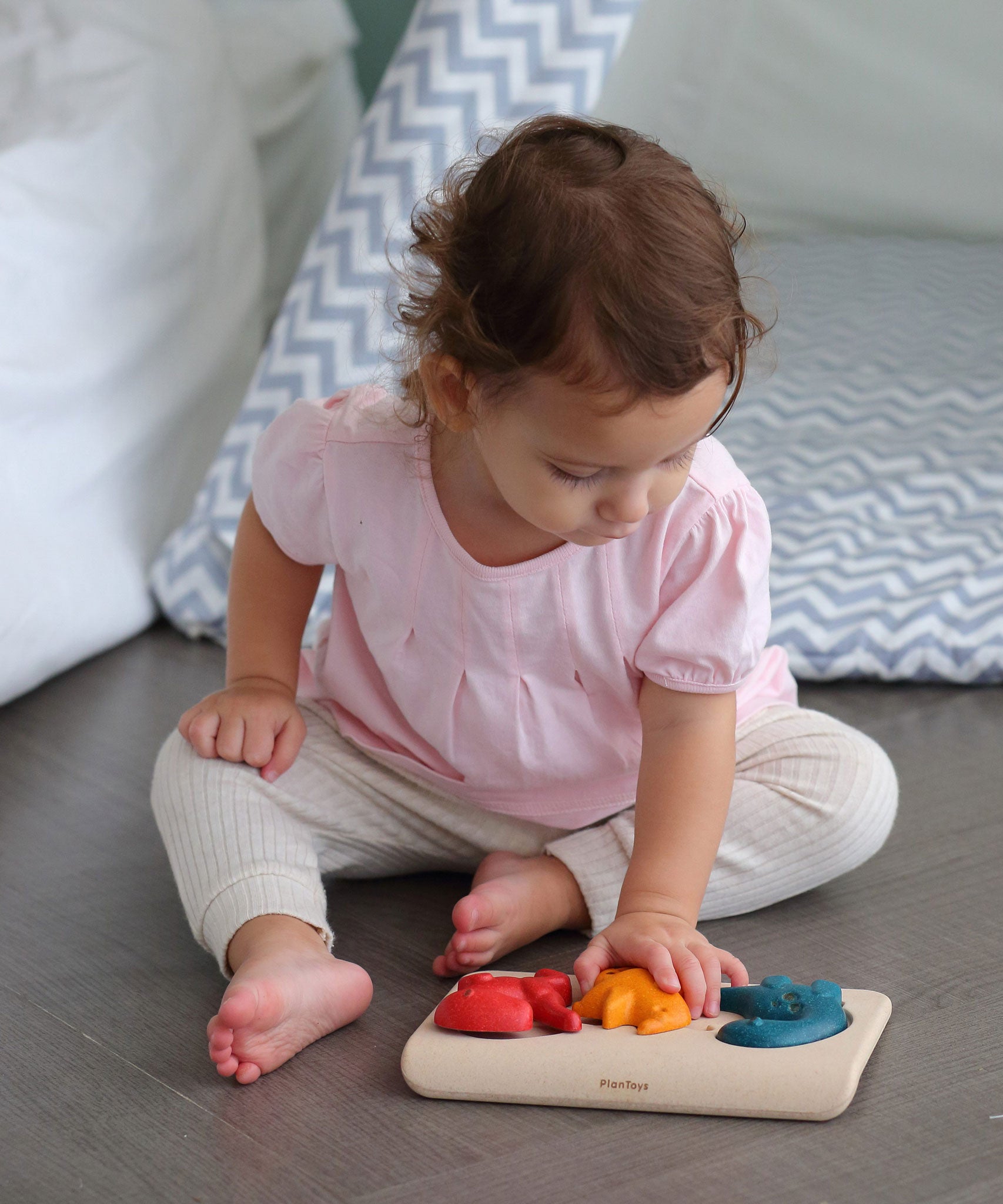 A child playing with PlanToys Dino Puzzle, child is sat on the floor. 