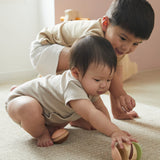 Two young children crawling on the floor reaching for the PlanToys clapping roller sensory toy. 