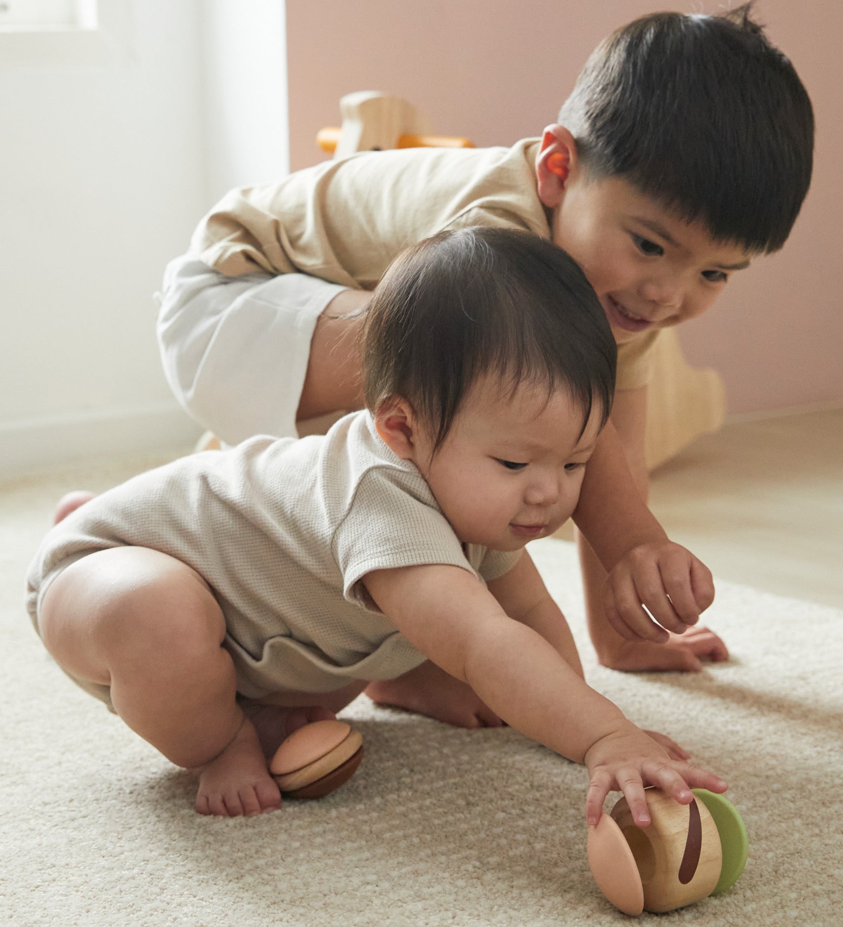 Two young children crawling on the floor reaching for the PlanToys clapping roller sensory toy. 