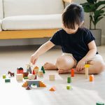 A child sitting on the floor playing with the PlanToys Countryside Blocks Set.