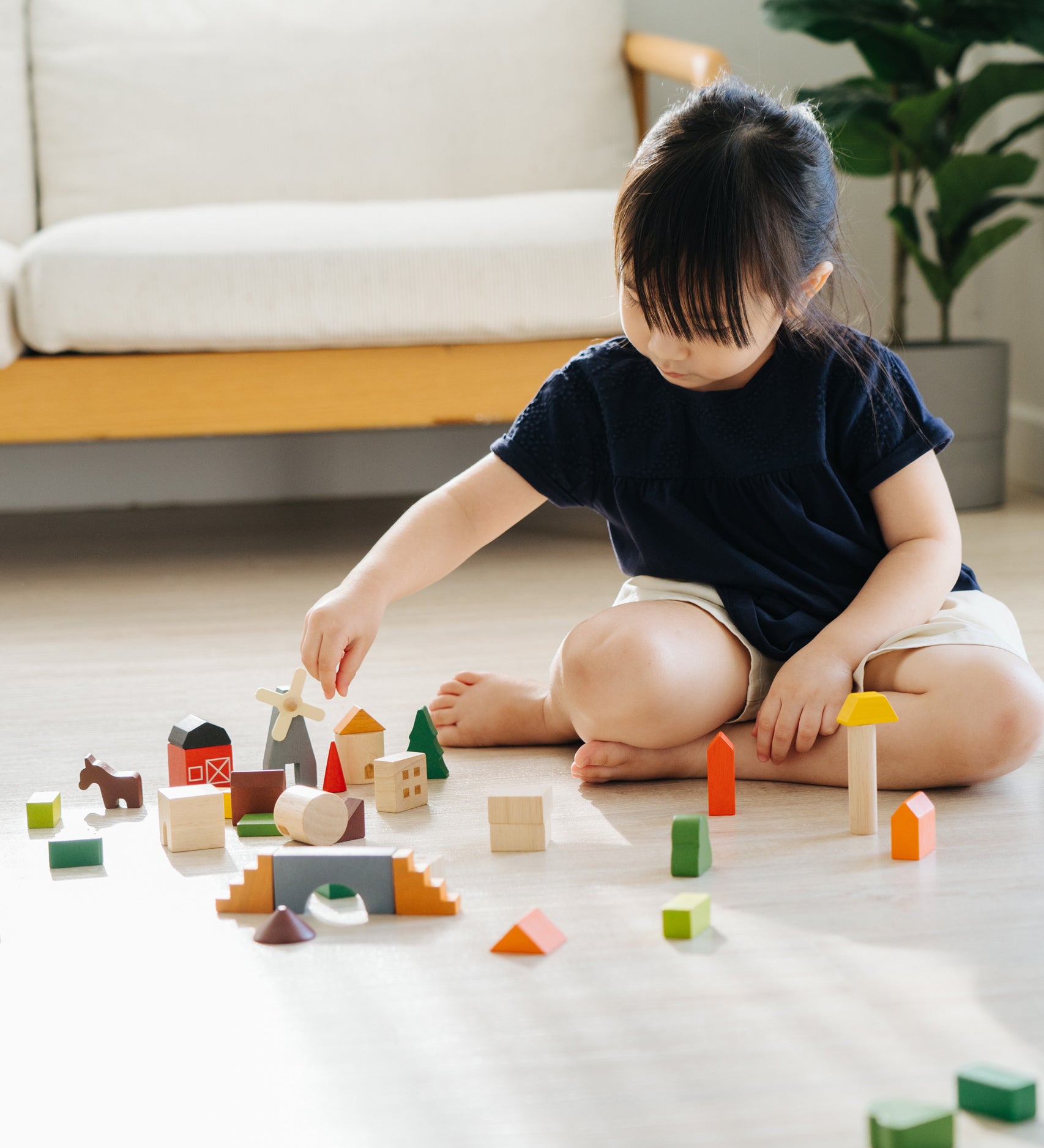 A child sitting on the floor playing with the PlanToys Countryside Blocks Set.