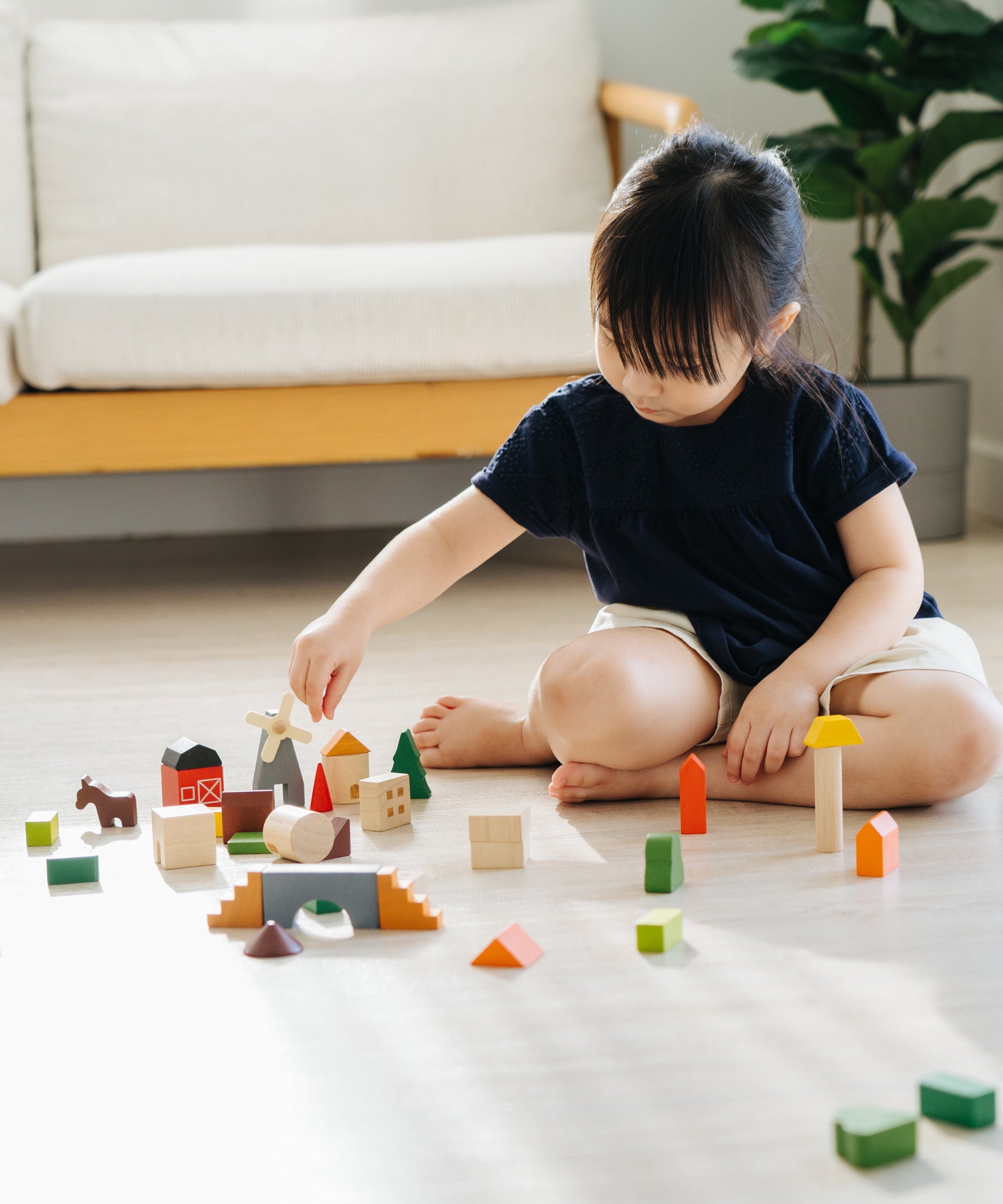 A child sitting on the floor playing with the PlanToys Countryside Blocks Set.