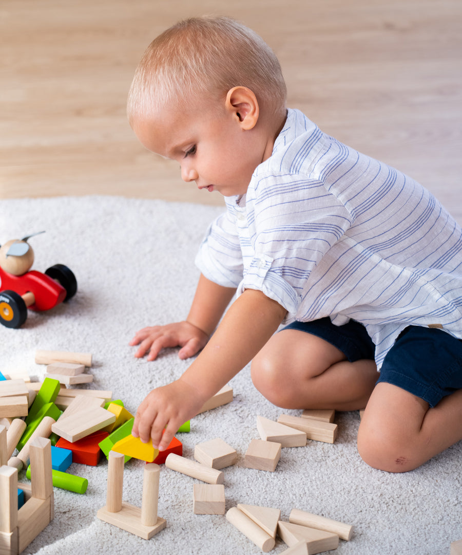 A child sat on a light grey coloured rug playing with the PlanToys 40 unit Colourful Block set. 