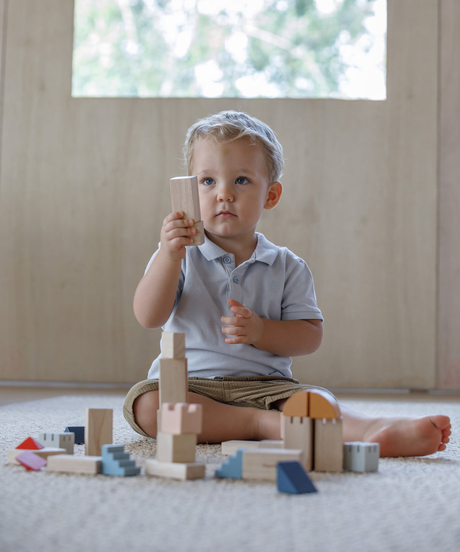 A child playing with the PlanToys Creative Blocks in the Orchard colour way. The child is sitting on a rug.  