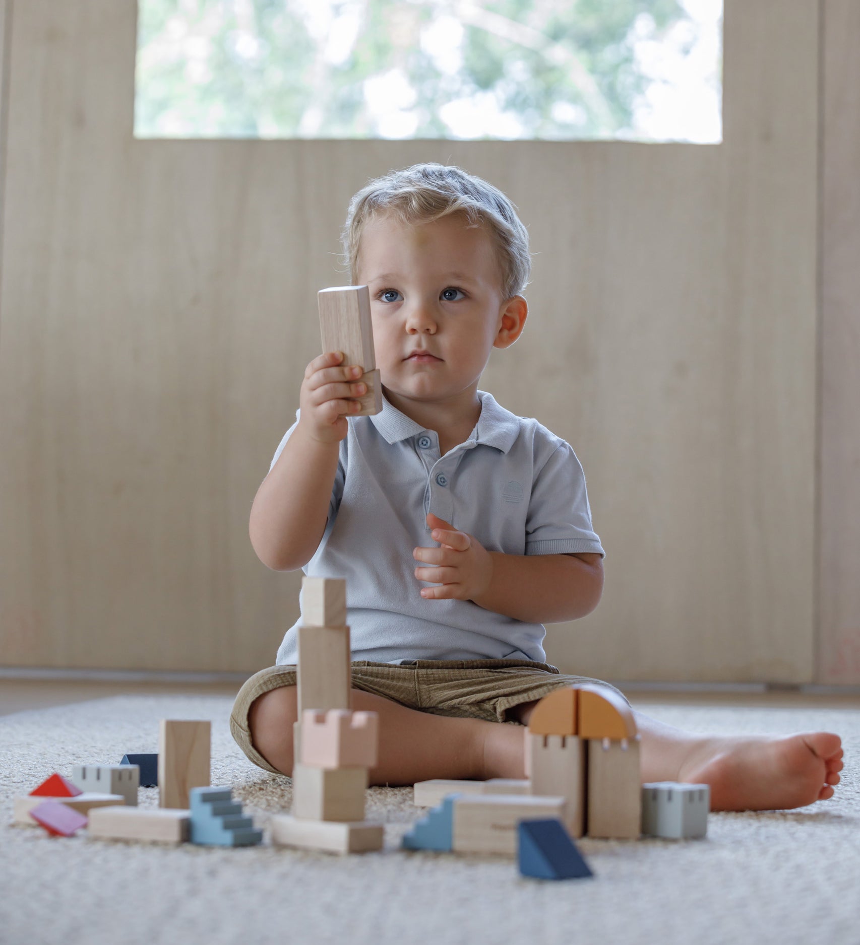 A child playing with the PlanToys Creative Blocks in the Orchard colour way. The child is sitting on a rug.  