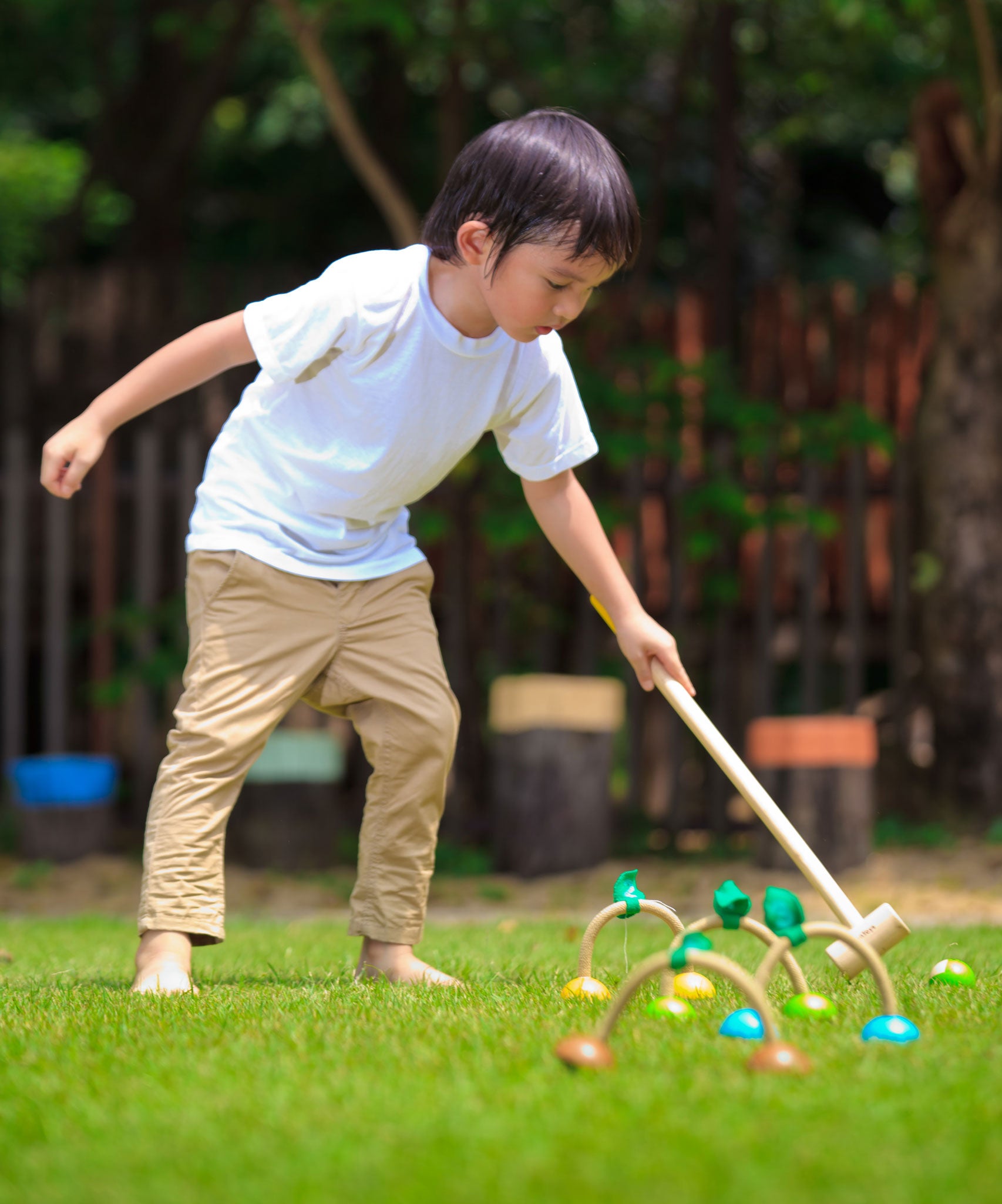 A child playing with the PlanToys Croquet set outdoors on a lawn. 