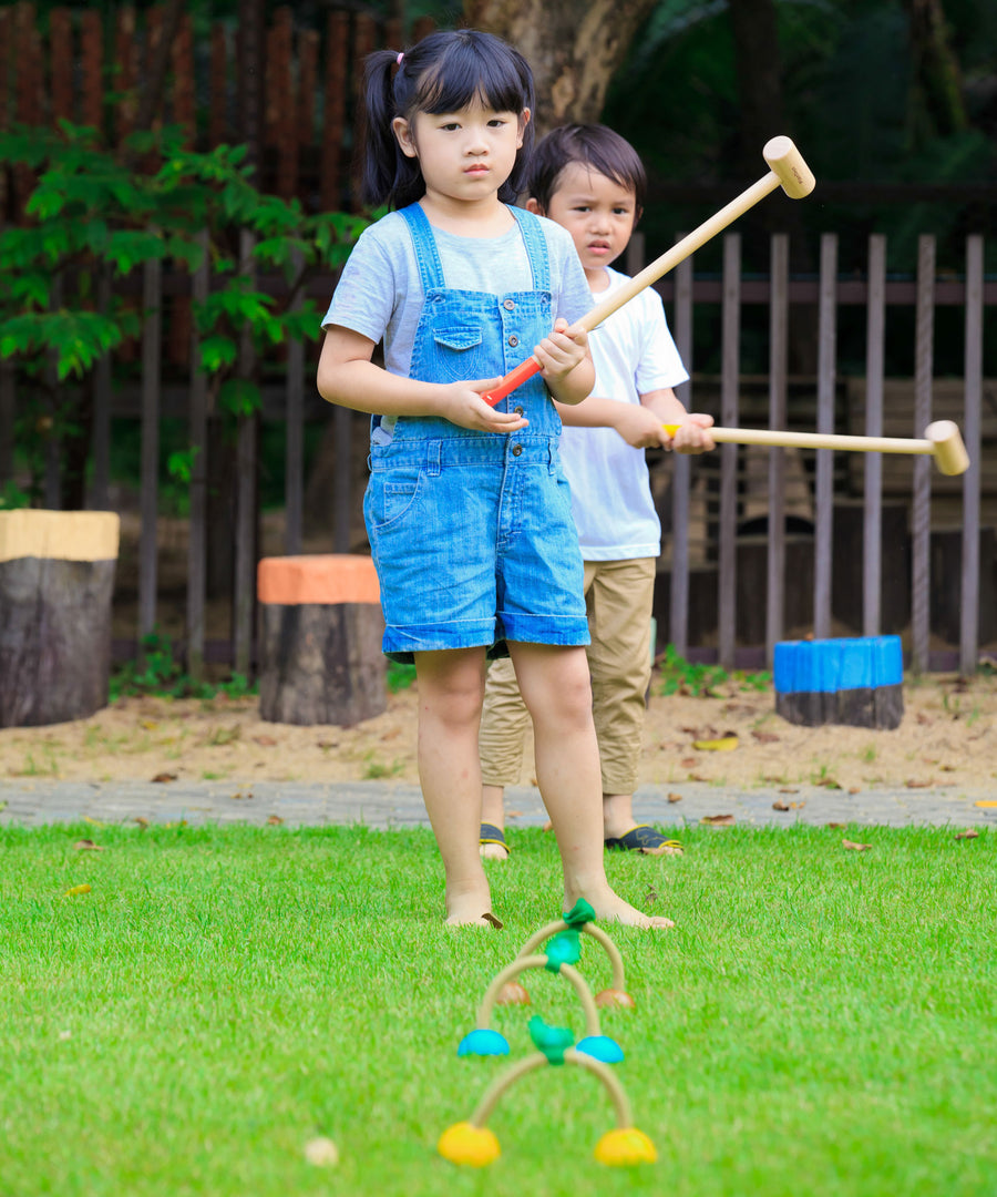 Children outdoors on a lawn with the  PlanToys Croquet set up in front of them. 