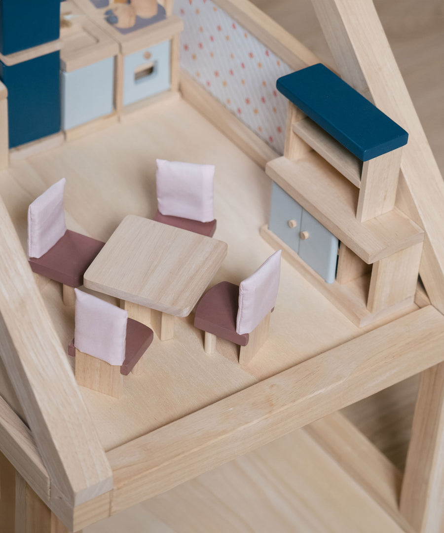 The pieces from the PlanToys Dining Room Dolls House Furniture set placed in a room in a wooden dolls house. 
