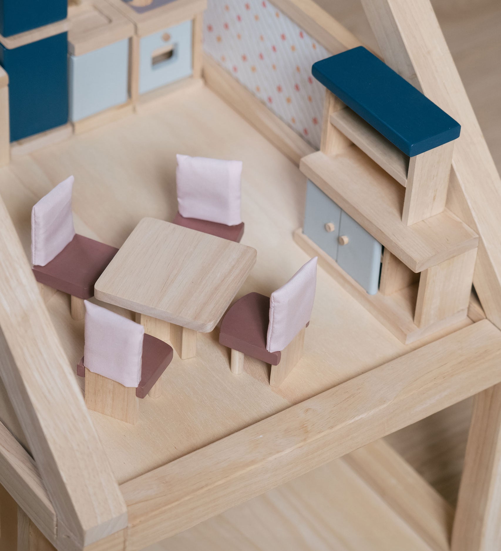 The pieces from the PlanToys Dining Room Dolls House Furniture set placed in a room in a wooden dolls house. 
