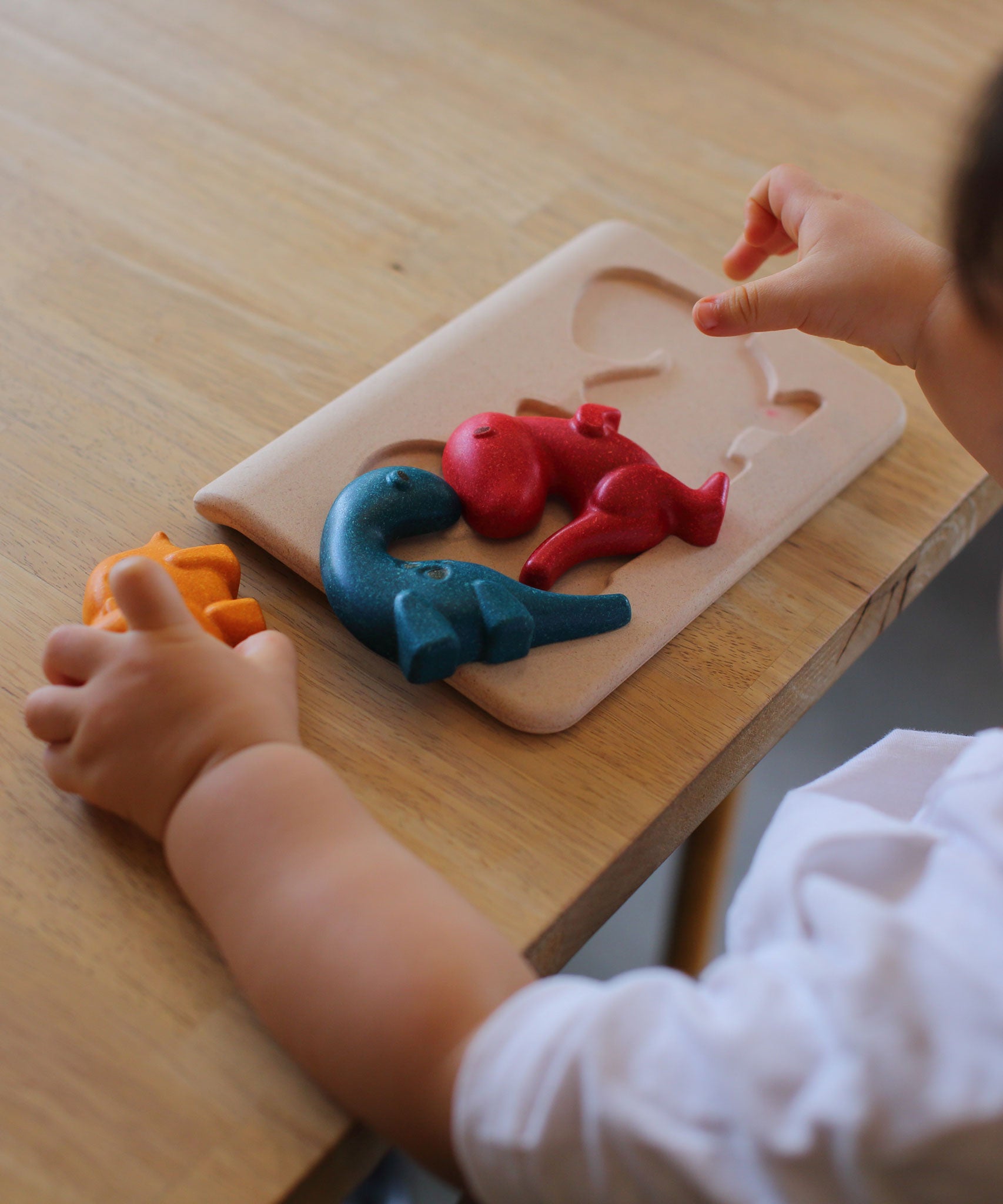 A close up of a child playing with the PlanToys Dino Puzzle on a wooden table. 