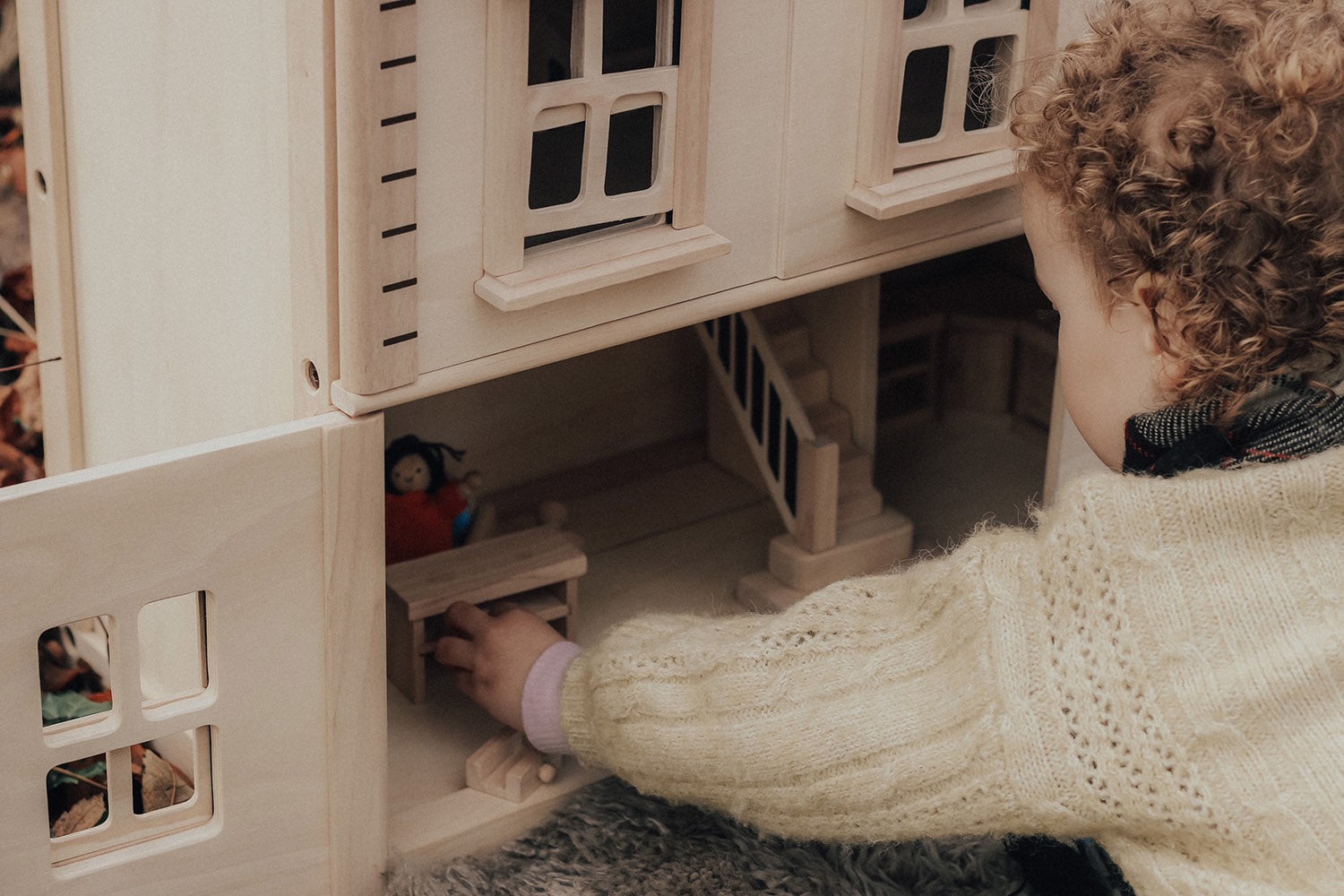 A close up of a child playing with the PlanToys Victorian Dolls House in a forest. 