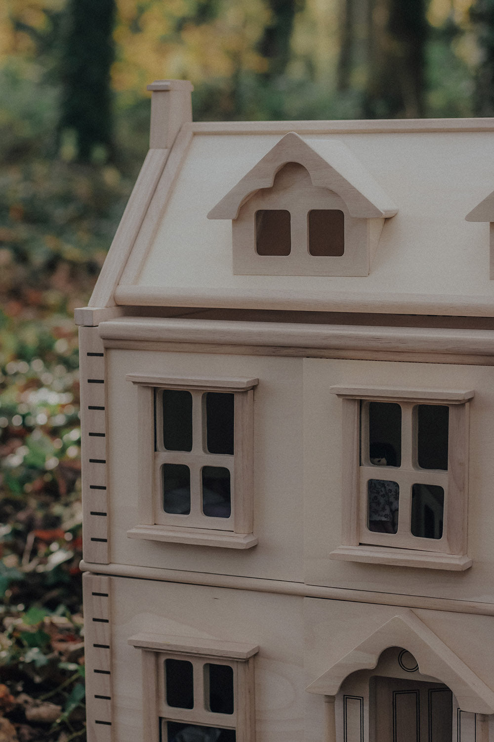 A close up of the corner of the PlanToys Victorian Dolls House in a forest. 